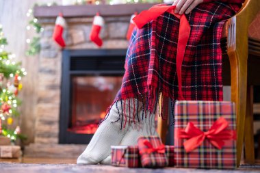 Koltuğunda oturan engelli kadınların çorapları şöminenin yanındaki ekoseyle kaplı ve Noel ağacı ve aile için hediye paketleri. Alt görünüm.