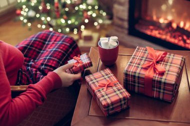 Yalnız bir kadın ekose kakaoyla kaplı, marşmelovla kaplı, uzak bir yer ve noel ağacının yanındaki koltukta oturuyor, aile için hediye paketlerini bitirdikten sonra rahatlıyor.