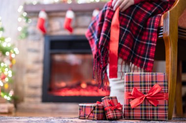 Kış çoraplarıyla kaplı kadın bacakları ekoseli oturma ve şöminenin yanındaki koltukta rahatlama ve aile için Noel ağacı paketleme kutuları. Alt görünüm.