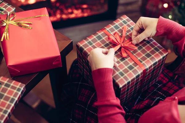 女人抱着巨大的礼品盒 坐在圣诞树旁和壁炉旁 包装手工制作的圣诞礼物 — 图库照片