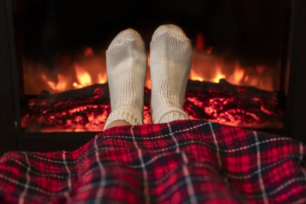 Woman legs in winter white socks covered christmas plaid near fireplace flame