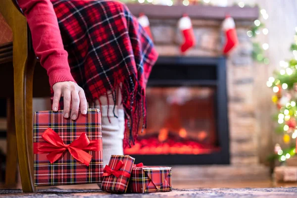 穿着冬季袜子的女人的腿被格子花覆盖着 坐在壁炉附近的扶手椅上 并为家人准备圣诞礼物盒 底部视图 — 图库照片
