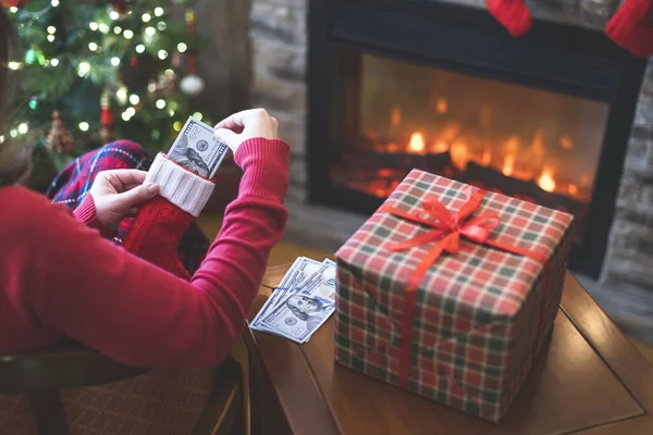 Женщина Кладет Американские Доллары Красный Рождественский Носок Сидит Рядом Елкой — стоковое фото