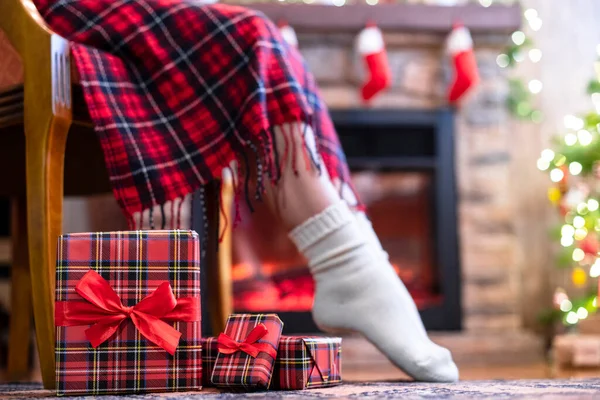 冬の靴下の女性の足は 暖炉の近くのアームチェアに座ってリラックスし 家族のためのクリスマスツリーのパッキングギフトボックスを果たしました 下の図 — ストック写真