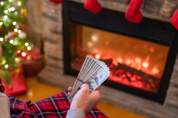 Мужчина Считает Американские Доллары Сидя Возле Рождественской Елки Камина Тратить — стоковое фото