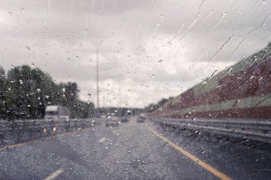 Arabanın ön camından yol manzarası ve sürat yaparken yağmur damlaları. Odaklanmamış otoyol. Sonbahar