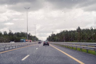 Arabanın ön camından yol manzarası ve sürat yaparken yağmur damlaları. Odaklanmamış otoyol. Sonbahar