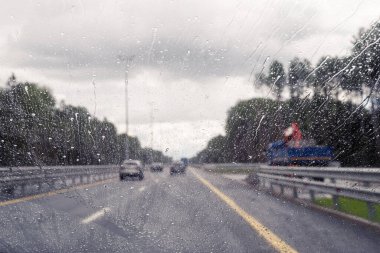 Arabanın ön camından yol manzarası ve sürat yaparken yağmur damlaları. Odaklanmamış otoyol. Sonbahar