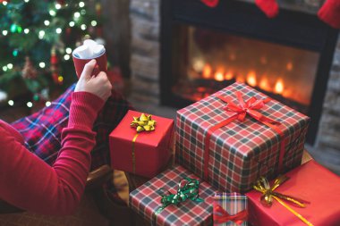 Aile için hediye paketlerini bitirdikten sonra, yalnız bir kadın ekose kakaoyla kaplı, marşmelovlu, uzak bir yer ve noel ağacının yanındaki koltukta oturup rahatlıyor.. 