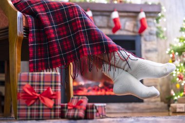Kış çoraplarıyla kaplı kadın bacakları ekoseli oturma ve şöminenin yanındaki koltukta rahatlama ve aile için Noel ağacı paketleme kutuları. Alt görünüm.