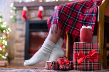 Çorapla kaplı kadın bacakları ekose oturma ve uzak bir yerin yanındaki koltukta rahatlama ve aile için paketleme paketlerini bitirdikten sonra bir fincan kakao ve marşmelov ile noel ağacı. Alt görünüm.
