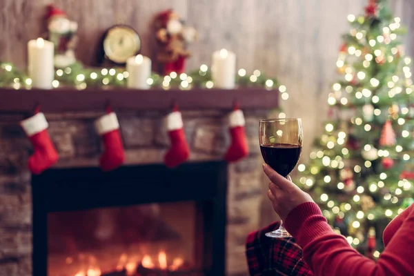 クリスマスのお別れの場所やモミの木の近くのアームチェアに座ってリラックスしたプレイカバーワインのガラスと女性の手 — ストック写真