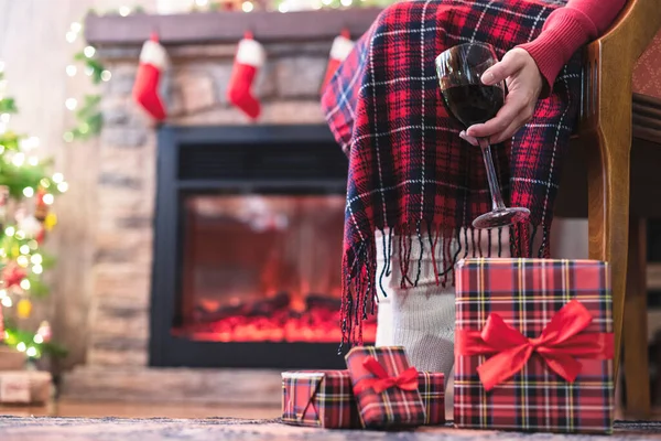 靴下に覆われた女性の足は 家族のためのパッキングギフトボックスを終えた後 別荘の近くのアームチェアとワインのグラスでクリスマスツリーに座ってリラックスしていました 下の図 — ストック写真