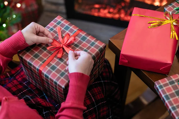 Woman holding huge gift box sitting near christmas tree and fireplace. Packing handmade christmas gifts .