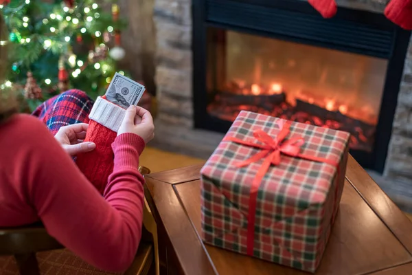 Женщина Кладет Американские Доллары Красный Рождественский Носок Сидит Рядом Елкой — стоковое фото