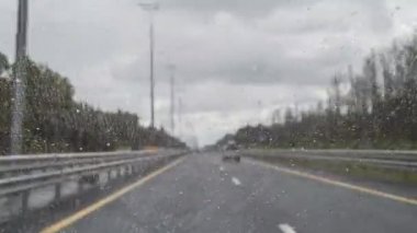 Araba sürüşü sırasında yağmur damlalarıyla birlikte arabanın ön camından geçen yol manzarasının orijinal hızlandırılmış videosu. Odaklanmamış otoyol. Sonbahar