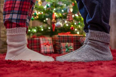 Kış çoraplarıyla ayak uçlarında duran kadın ayakları, hediyelerle dolu bir Noel ağacının yanındaki tüylü kırmızı bir battaniyenin üzerinde duruyor. Kavram 