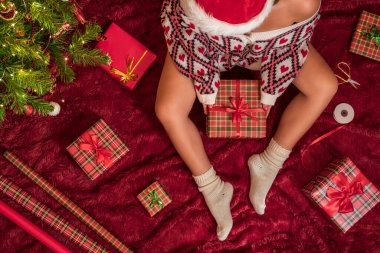 Kırmızı Noel Baba şapkalı bir kadının, Noel ağacının yanındaki kabarık ekose kumaşta oturan aile için Noel hediyesi kutularını paketlediği en iyi manzara. Düz yatıyordu.