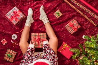 Kırmızı Noel Baba şapkalı bir kadının, Noel ağacının yanındaki kabarık ekose kumaşta oturan aile için Noel hediyesi kutularını paketlediği en iyi manzara. Düz yatıyordu.