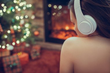 Kulaklıklı kadın kış akşamı şömine ateşi ve yılbaşı ağacının yanında oturup ısınıyor..