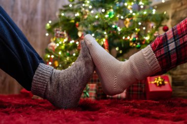 Kış çoraplarının içindeki erkek ve kadın ayakları birbirine dokunuyor. Noel ağacının yanında hediyelerle oturan adam ve kadın. Kavram