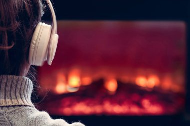Kulaklıklı kadın kış akşamı şömine ateşinin yanında oturup ısınıyor..
