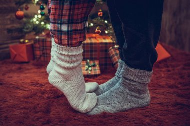 Kış çoraplarıyla ayak uçlarında duran kadın ayakları, hediyelerle dolu bir Noel ağacının yanındaki tüylü kırmızı bir battaniyenin üzerinde duruyor. Kavram 