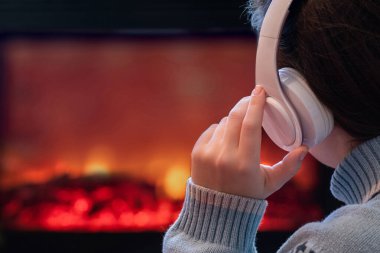 Kulaklıklı kadın kış akşamı şömine ateşinin yanında oturup ısınıyor..