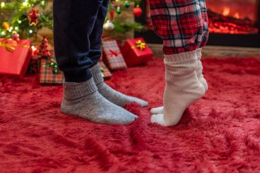 Kış çoraplarının içinde ayak uçlarında duran kadın ayakları, hediyelerle dolu bir Noel ağacının yanındaki tüylü kırmızı bir battaniyenin üzerinde duruyor. Kavram 