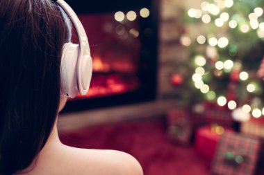 Kulaklıklı kadın kış akşamı şömine ateşi ve yılbaşı ağacının yanında oturup ısınıyor..