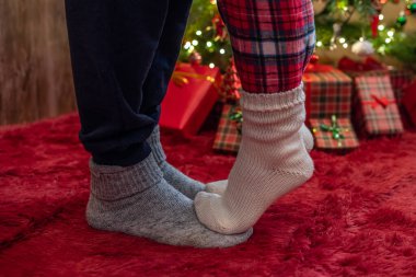 Kış çoraplarıyla ayak uçlarında duran kadın ayakları, hediyelerle dolu bir Noel ağacının yanındaki tüylü kırmızı bir battaniyenin üzerinde duruyor. Kavram 