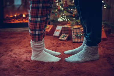 Kış çoraplarıyla ayak uçlarında duran kadın ayakları, hediyelerle dolu bir Noel ağacının yanındaki tüylü kırmızı bir battaniyenin üzerinde duruyor. Kavram 