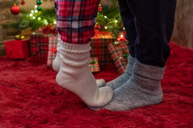 Kış çoraplarıyla ayak uçlarında duran kadın ayakları, hediyelerle dolu bir Noel ağacının yanındaki tüylü kırmızı bir battaniyenin üzerinde duruyor. Kavram 