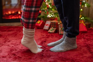 Kış çoraplarının içinde ayak uçlarında duran kadın ayakları, hediyelerle dolu bir Noel ağacının yanındaki tüylü kırmızı bir battaniyenin üzerinde duruyor. Kavram 