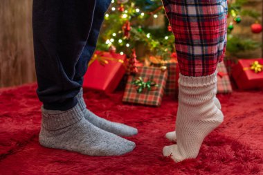 Kış çoraplarının içinde ayak uçlarında duran kadın ayakları, hediyelerle dolu bir Noel ağacının yanındaki tüylü kırmızı bir battaniyenin üzerinde duruyor. Kavram 