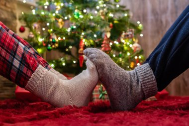 Kış çoraplarının içindeki erkek ve kadın ayakları birbirine dokunuyor. Noel ağacının yanında hediyelerle oturan adam ve kadın. Kavram
