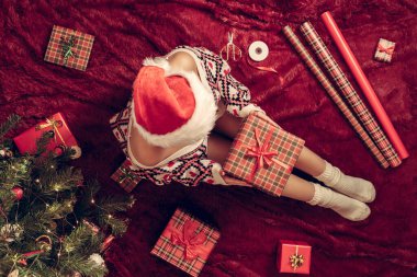 Dizlerinin üzerinde Noel hediyesi kutusu olan bir kadının en iyi görüntüsü. Noel ağacının yanındaki kabarık ekose üzerinde oturan aile için kadın paketleme hediyeleri. Düz yatıyordu.