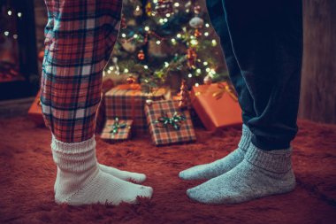 Kış çoraplarıyla ayak uçlarında duran kadın ayakları, hediyelerle dolu bir Noel ağacının yanındaki tüylü kırmızı bir battaniyenin üzerinde duruyor. Kavram 
