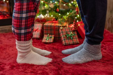 Kış çoraplarıyla ayak uçlarında duran kadın ayakları, hediyelerle dolu bir Noel ağacının yanındaki tüylü kırmızı bir battaniyenin üzerinde duruyor. Kavram 