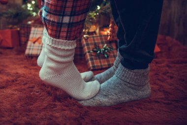 Kış çoraplarıyla ayak uçlarında duran kadın ayakları, hediyelerle dolu bir Noel ağacının yanındaki tüylü kırmızı bir battaniyenin üzerinde duruyor. Kavram 