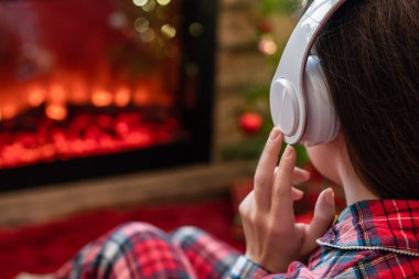 Kulaklıklı bir kadın kış akşamı şömine ateşi ve noel ağacının yanında oturup ısınıyor..