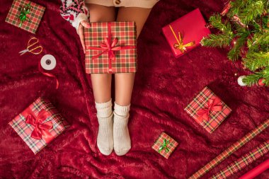 Dizlerinin üzerinde Noel hediyesi kutusu olan bir kadının en iyi görüntüsü. Noel ağacının yanındaki kabarık ekose üzerinde oturan aile için kadın paketleme hediyeleri. Düz yatıyordu.