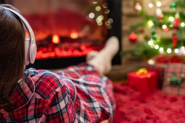 冬天的晚上 穿着睡衣 头戴耳机的女人躺在壁炉边 放松暖和 — 图库照片