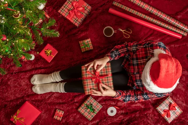 膝の上にクリスマスギフトボックスを持つ女性のトップビュー クリスマスツリーの近くで遊ぶふわふわの上に座っている家族のための女性の包装ギフト — ストック写真