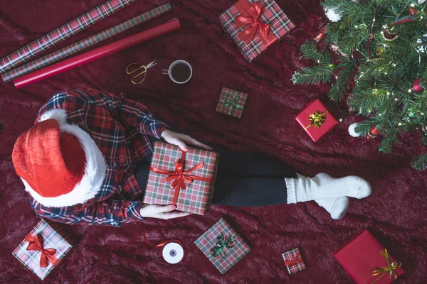 膝の上にクリスマスギフトボックスを持つ女性のトップビュー クリスマスツリーの近くで遊ぶふわふわの上に座っている家族のための女性の包装ギフト — ストック写真