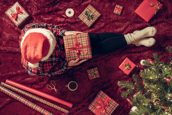 膝の上にクリスマスギフトボックスを持つ女性のトップビュー クリスマスツリーの近くで遊ぶふわふわの上に座っている家族のための女性の包装ギフト — ストック写真