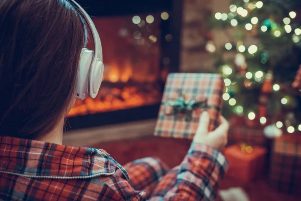女性でパジャマでクリスマスギフトボックスで手に座ってふわふわ暖炉とクリスマスツリーの近くで再生 — ストック写真