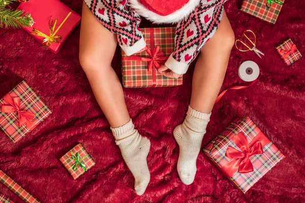 Kırmızı Noel Baba şapkalı bir kadının, Noel ağacının yanındaki kabarık ekose kumaşta oturan aile için Noel hediyesi kutularını paketlediği en iyi manzara. Düz yatıyordu.