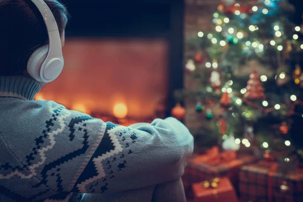 冬天的傍晚 坐在壁炉边的火焰和圣诞树旁 一个人坐在耳机里 暖烘烘 — 图库照片