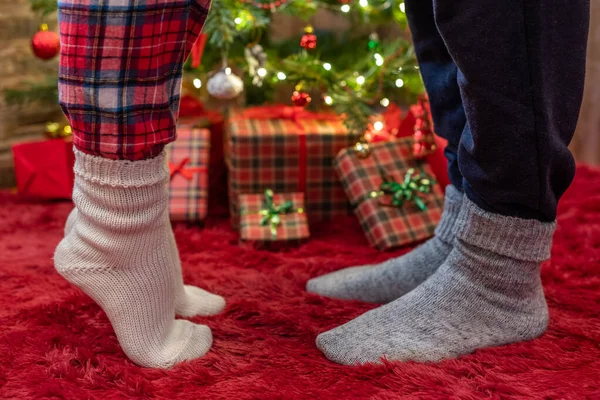 Woman feet standing in tip toe in winter socks near male lags on a fluffy red blanket near a Christmas tree with gifts. Concept